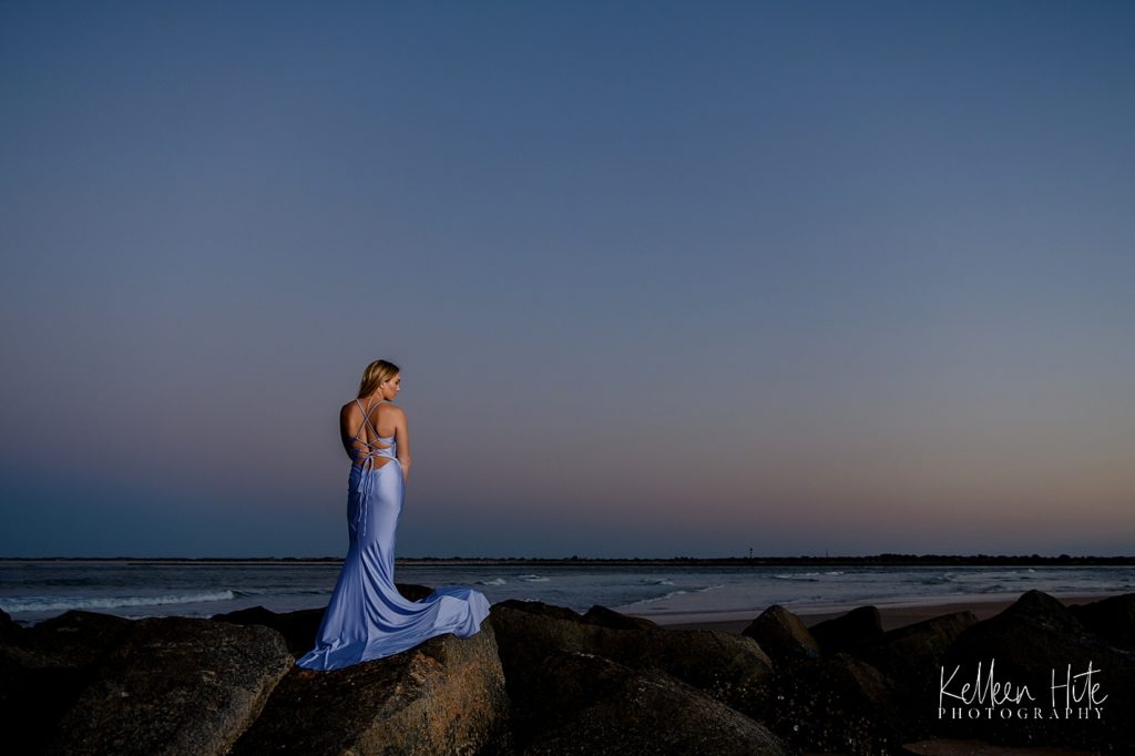 senior on rocks by peach in prom dress at sunet